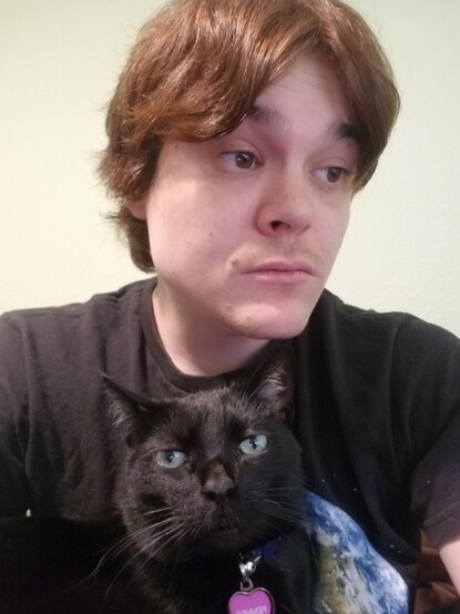 rye, red hair parted down the middle, looks to their left while their black cat fennec sits in their lap and looks at the camera